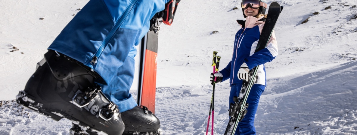 Skifahrer stehen nebeneinander auf einer verschneiten Piste vor alpiner Bergkulisse.